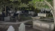 The image captures a nighttime scene of an old cemetery with tombstones and graves illuminated by faint lighting.