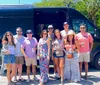 A group of people are posing for a photo in front of a black van on a sunny day appearing to be in a cheerful and casual mood