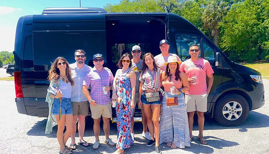 A group of people are posing for a photo in front of a black van on a sunny day, appearing to be in a cheerful and casual mood.