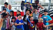 A group of children dressed in pirate attire are enthusiastically shouting and posing, with one holding a Jolly Roger flag, during what appears to be a themed party or event.