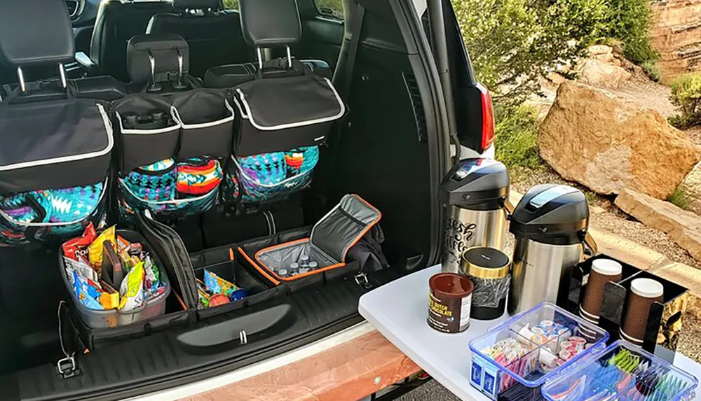 The image depicts a well-organized car trunk with various supplies and food items likely prepared for a road trip or outdoor excursion