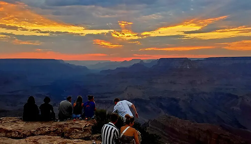 A group of people enjoys a breathtaking sunset at the Grand Canyon with vibrant colors painting the sky and silhouetting the canyons vast rugged landscape