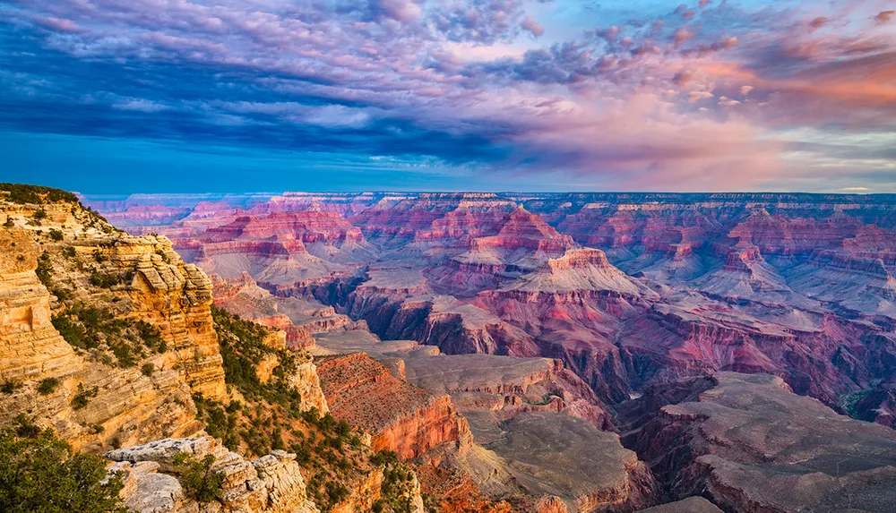 The image showcases a breathtaking view of the Grand Canyon bathed in the warm glow of sunset with a tapestry of rich colors and dramatic cliffs under a dynamic and colorful sky