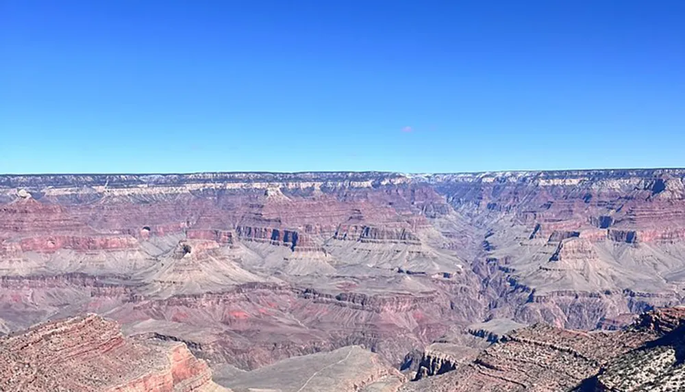 The image showcases the vast and colorful geological formations of the Grand Canyon under a clear blue sky