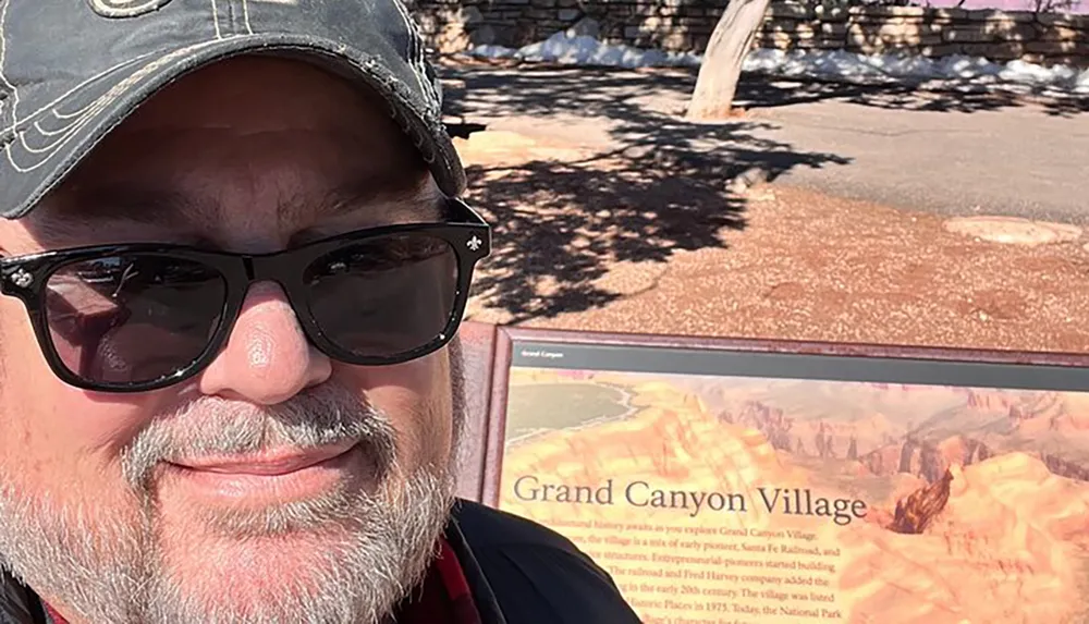 A person is taking a selfie with sunglasses on in front of a sign that reads Grand Canyon Village