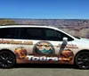 A tour vehicle with a custom wrap advertising Grand Canyon Explorer Tours is parked in front of a scenic view of the Grand Canyon