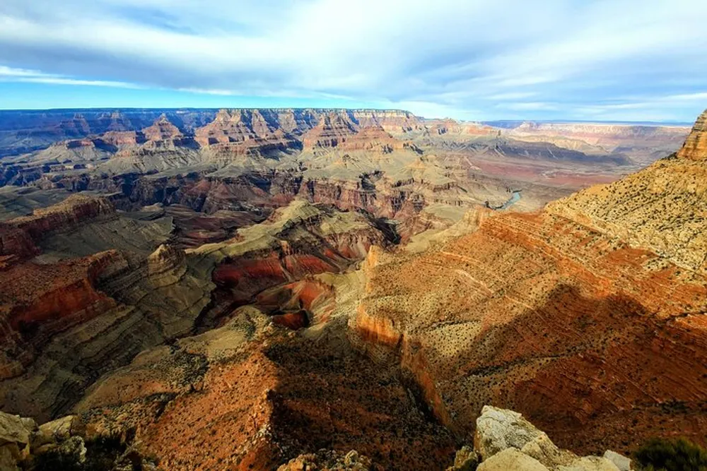 The image shows the expansive and colorful landscape of the Grand Canyon under a partly cloudy sky