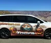 A tour van featuring advertising graphics is parked in front of the Grand Canyon