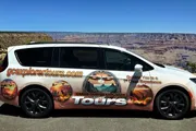 A tour van featuring advertising graphics is parked in front of the Grand Canyon.