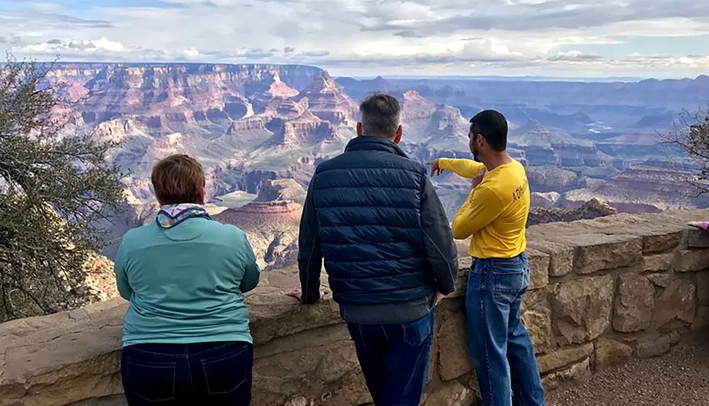 Three people are standing at an overlook admiring the vast scenic view of the Grand Canyon