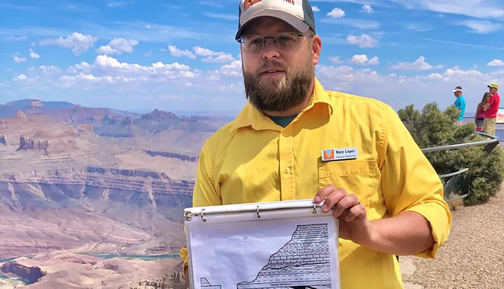 A person is holding a clipboard with geological information in front of a scenic view of the Grand Canyon