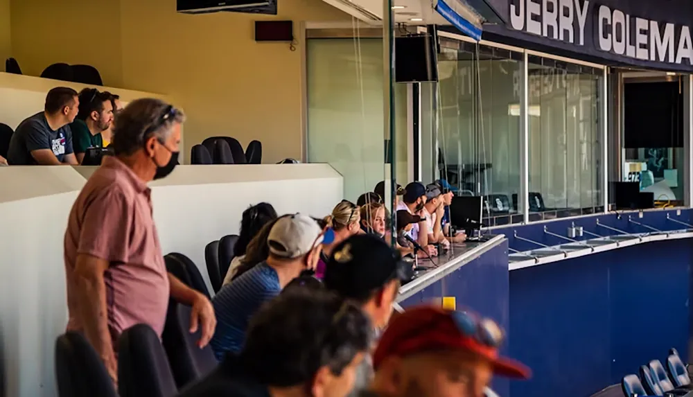 A group of people are seated in a stadium box area some wearing masks watching an event