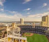 The image shows a panoramic view of a baseball stadium surrounded by city buildings and water under a partly cloudy sky