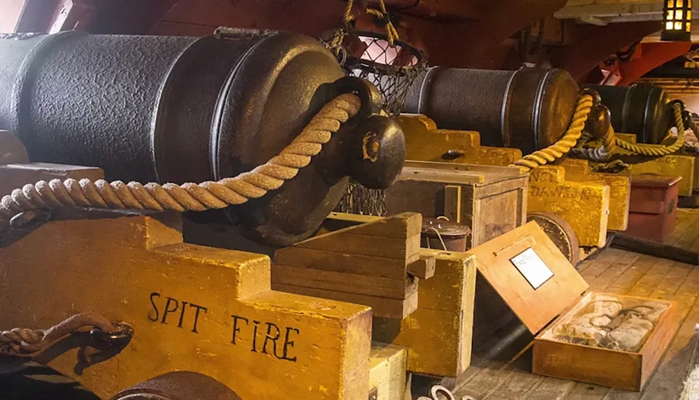 The image shows a row of vintage cannons in a ships interior with one labeled Spit Fire