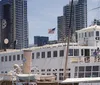 The image depicts the historic steam ferry Berkeley docked with several people aboard set against a backdrop of modern high-rise buildings and an American flag