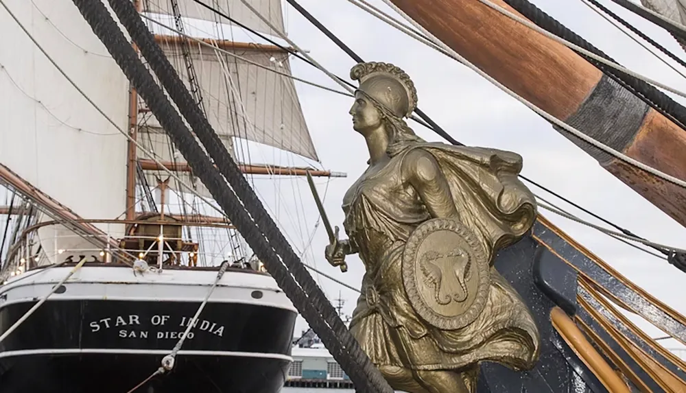 The image shows the figurehead of the historic sailing ship Star of India with its intricate rigging and sails visible in the background