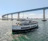 A cruise ship named Admiral Hornblower sails under a large bridge with a scenic shoreline in the background while an inset shows a bottle of Chandon champagne on a table set with food