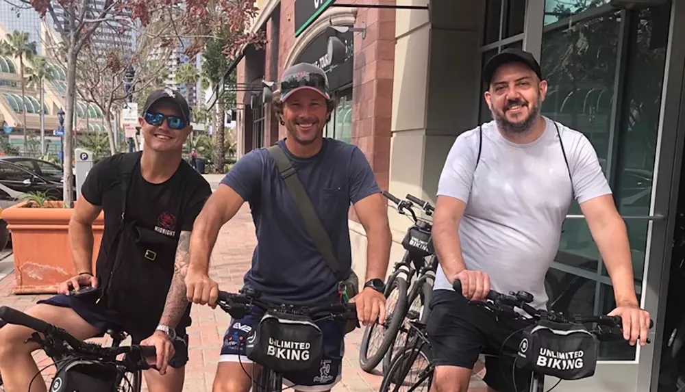 Three people are smiling and posing with bicycles on a city street