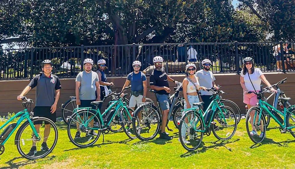 A group of eight people wearing helmets pose with their bicycles on a sunny day