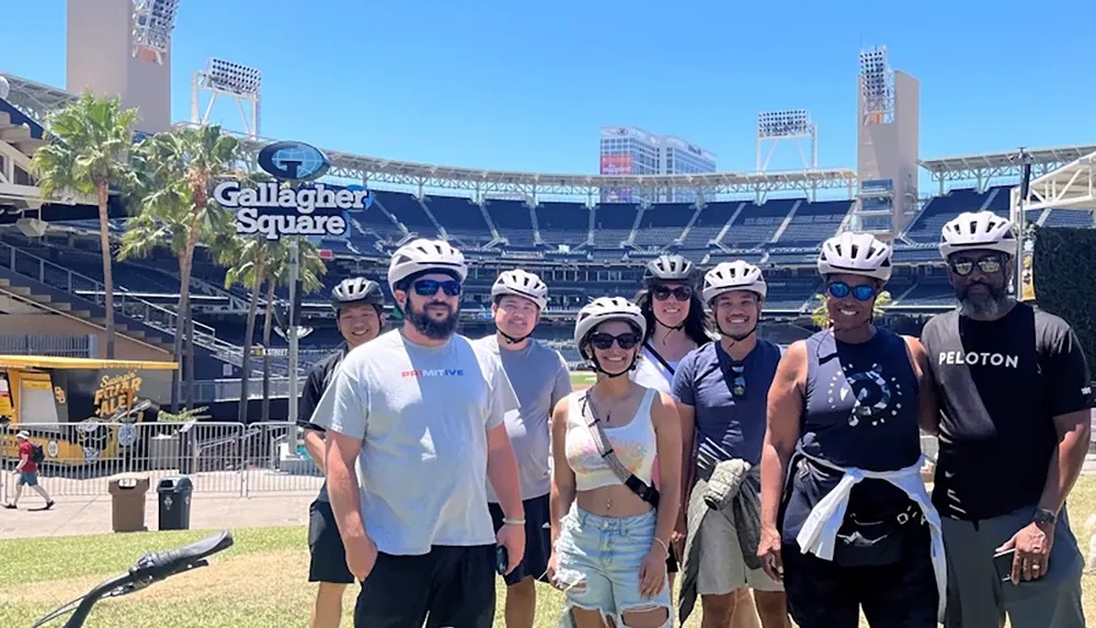 A group of people wearing helmets pose together in front of Gallagher Square at an outdoor stadium