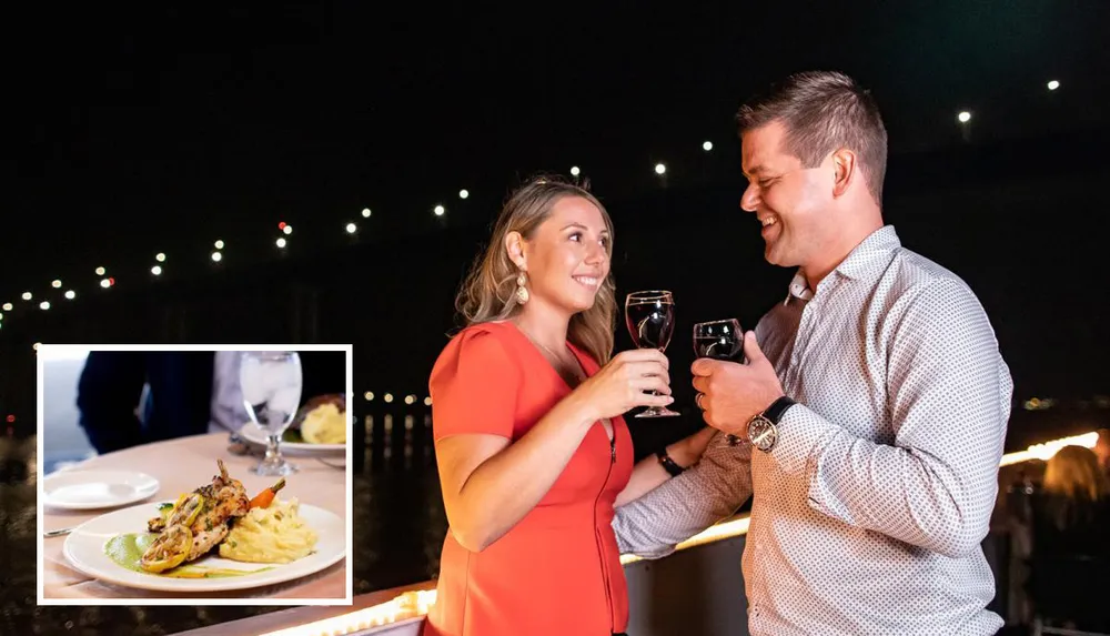 A couple is toasting with wine glasses at a nighttime outdoor setting with a plated dish of food inset in the image