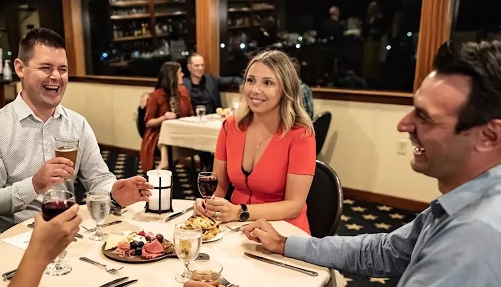 Four people are enjoying drinks and food together at a restaurant laughing and chatting