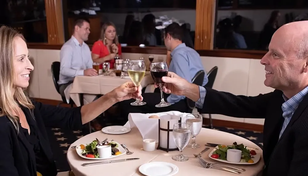 A couple is clinking glasses in a restaurant while other diners are seated in the background