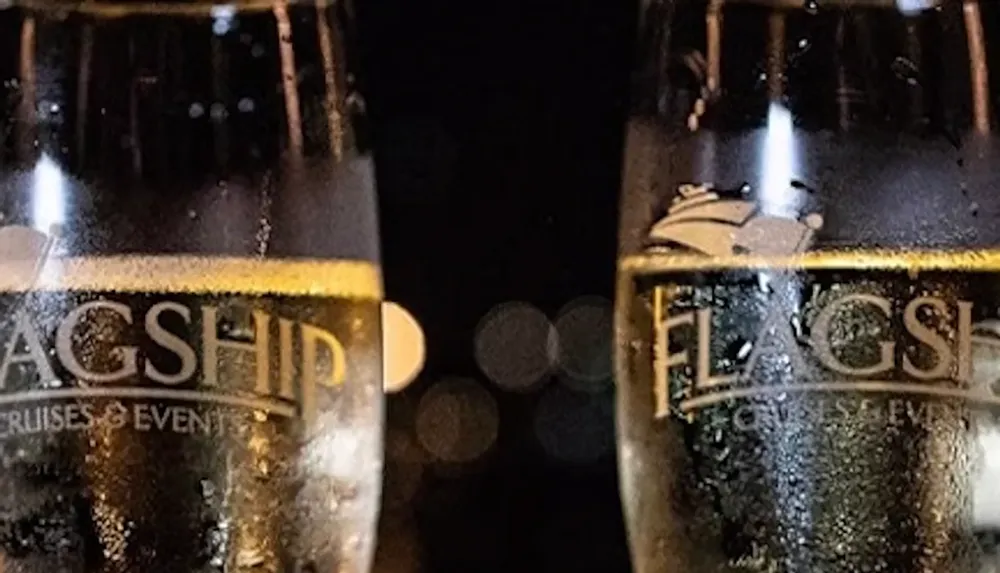 Two champagne glasses with Flagship Cruises  Events printed on them are partially filled and pictured against a dark background with bokeh lights