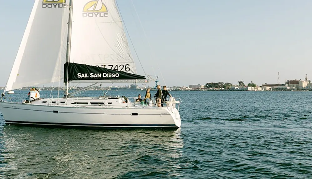 A sailboat with several people on board is cruising in a calm body of water near San Diego