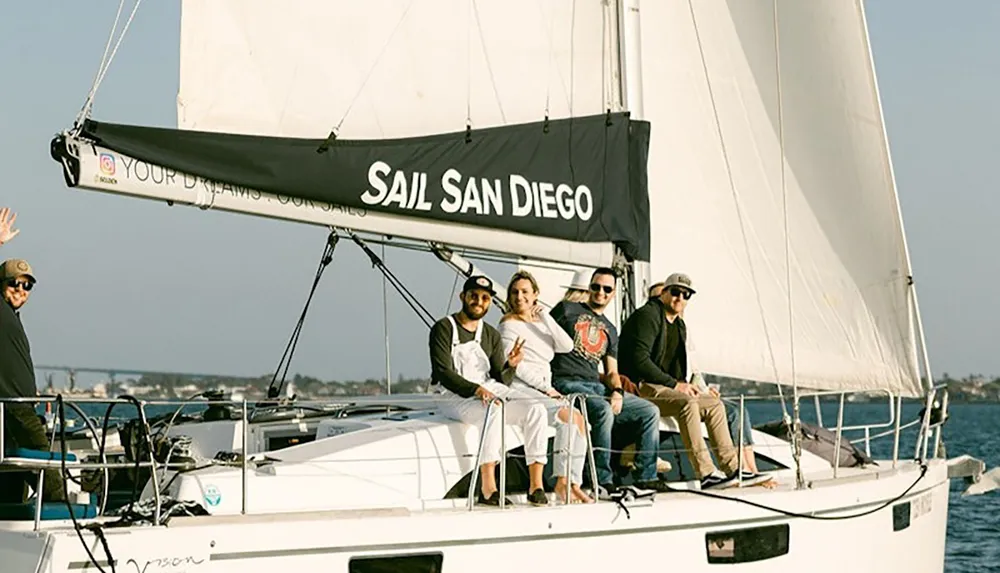 A group of people are sitting on a sailboat with a sail labeled Sail San Diego on a sunny day