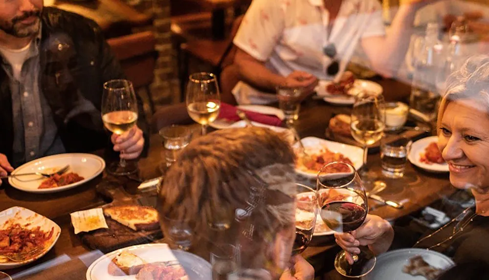 A group of people enjoying a meal together at a restaurant table with wine glasses and various dishes in front of them