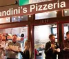 People are enjoying pizza outside Landinis Pizzeria under a warmly lit sign