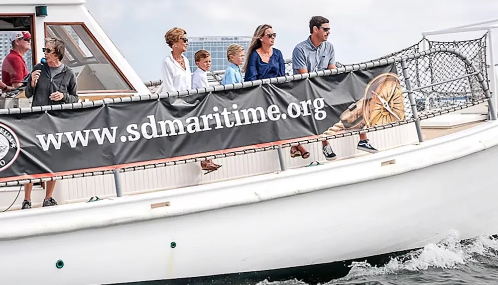 A group of people are standing on a boat with a banner displaying wwwsdmaritimeorg on the side