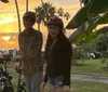 Four people are riding bicycles along a coastal road with palm trees and parked cars in the background