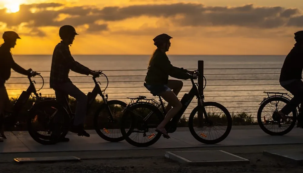 Four people are riding bikes by the ocean at sunset