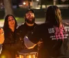 A group of people is gathered outdoors at night laughing and enjoying each others company around a light source