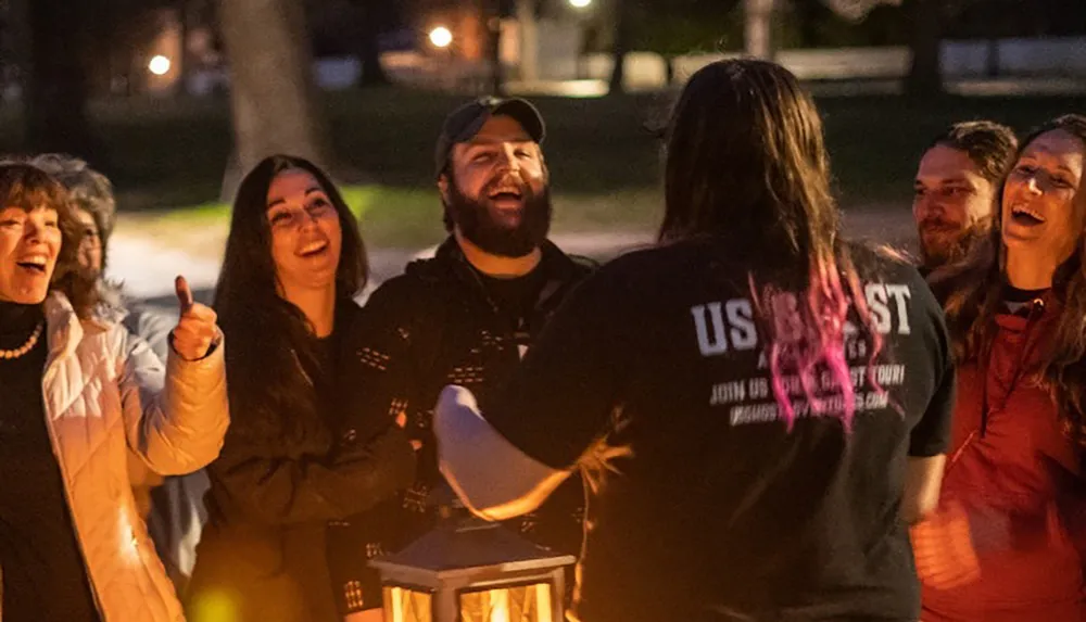 A group of people is gathered outdoors at night laughing and enjoying each others company around a light source