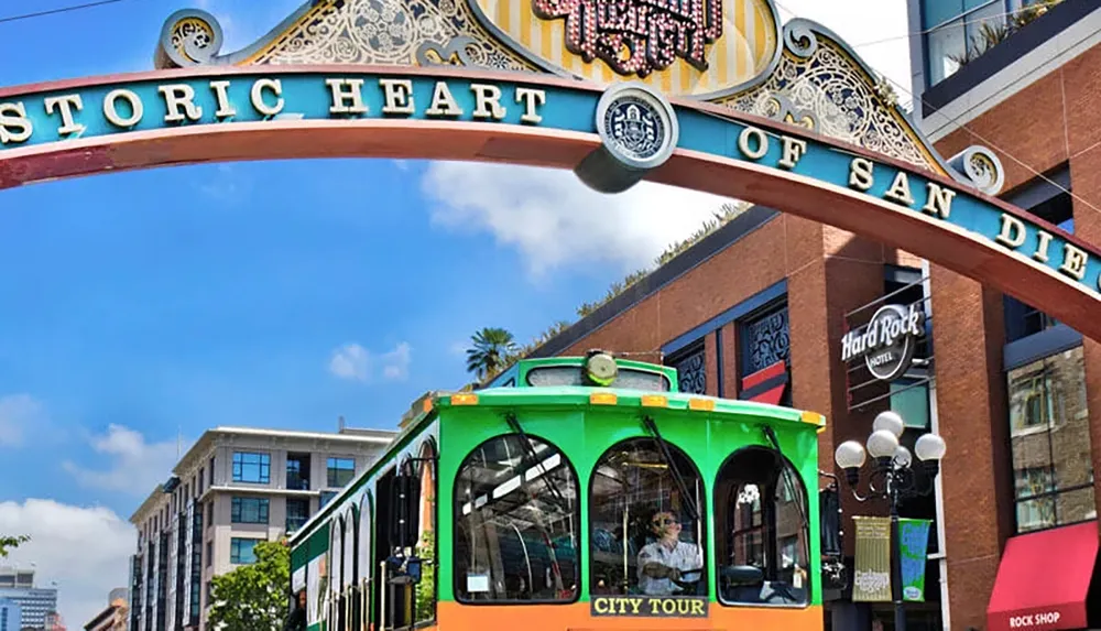 A city tour trolley passes under the Historic Heart of San Diego arch in a vibrant urban setting