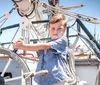 A young boy is steering a ships wheel on a sailboat under a clear blue sky