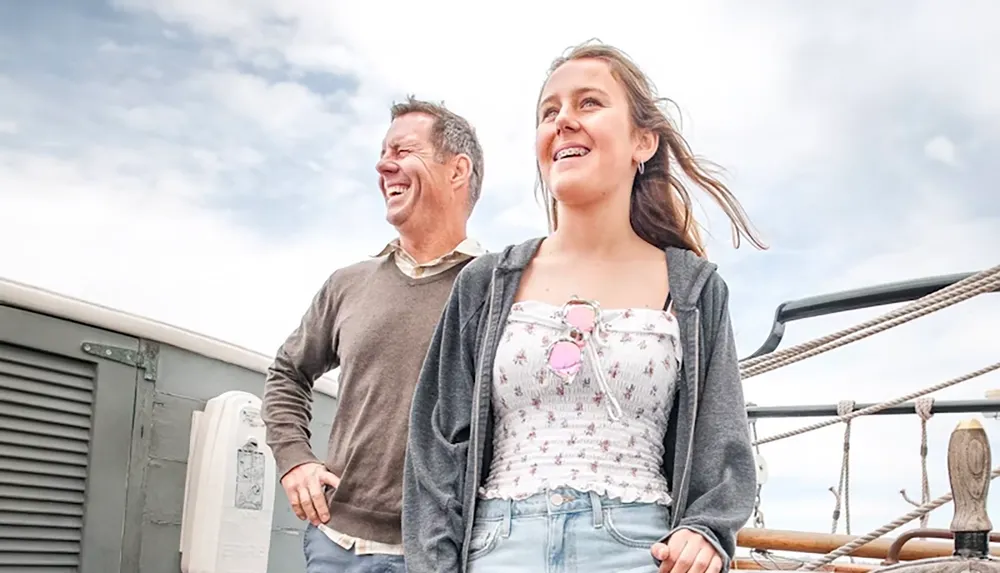 A man and a young woman are smiling joyfully while standing on a boat