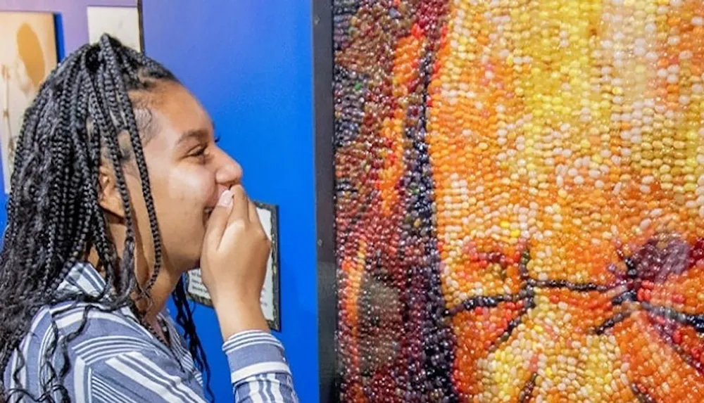 A person is smiling while looking closely at a colorful artwork made of jelly beans