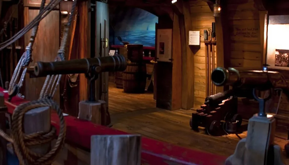 The image shows the interior of a historical ship exhibit featuring wooden beams nautical ropes cannons and barrels