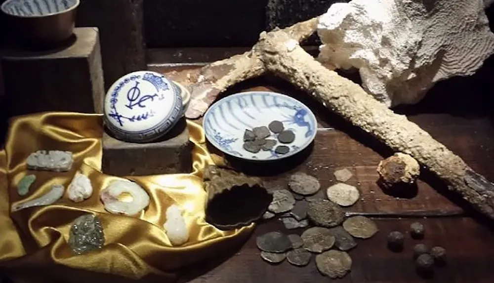 The image displays a collection of assorted artifacts including coins pottery fragments and minerals arranged on a wooden surface adorned with a golden fabric