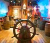 The image depicts a colorful interactive pirate ship exhibit with a ships wheel barrels and nautical decorations