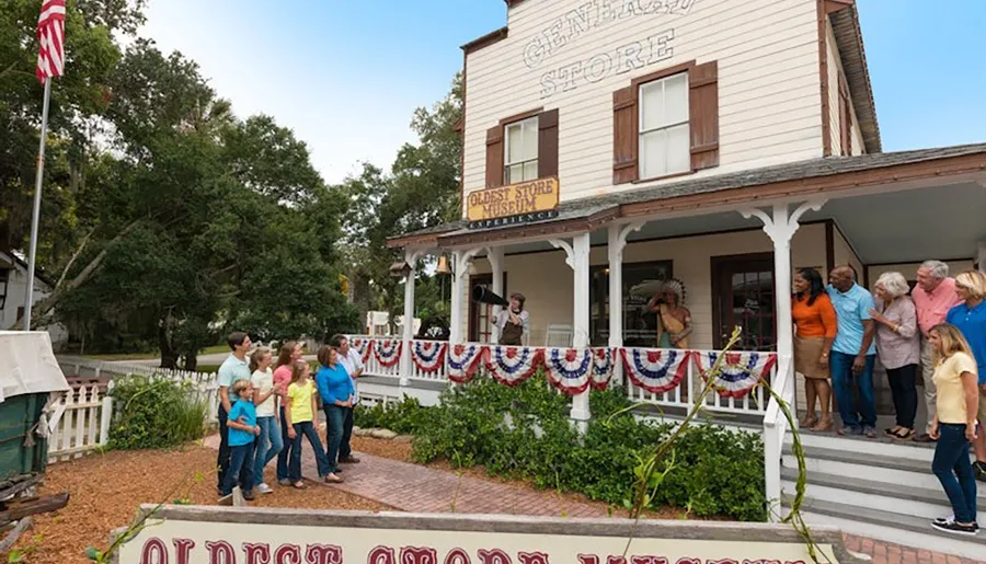 A group of people stand outside an old-fashioned general store, decorated with bunting, for a Oldest Store Museum experience.