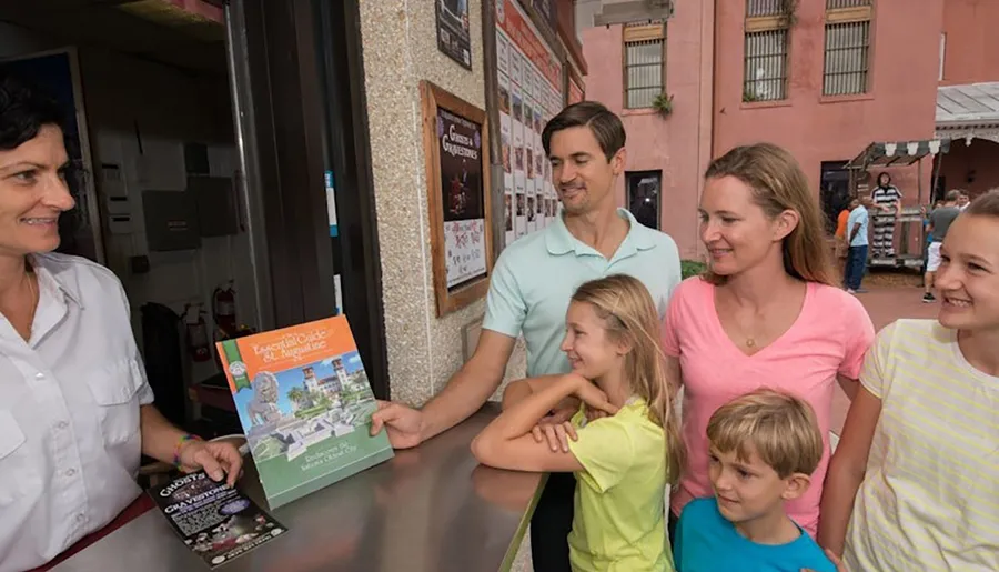 A family is smiling and receiving a brochure from a staff member at a ticket counter.