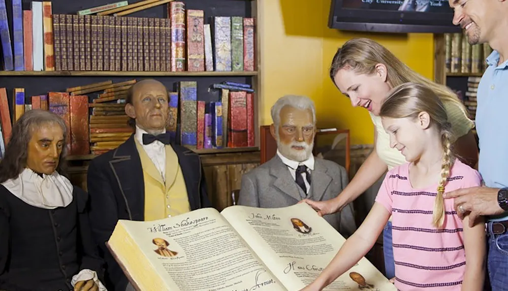 A family is interacting with a large open book in a library setting surrounded by lifelike wax figures of historical figures