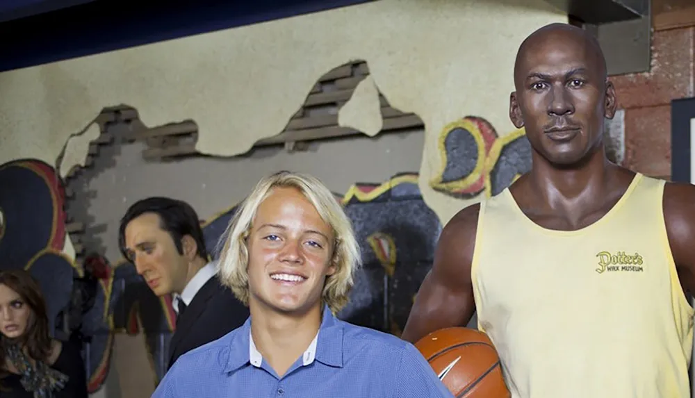 A person is posing next to a wax figure of a basketball player at a wax museum