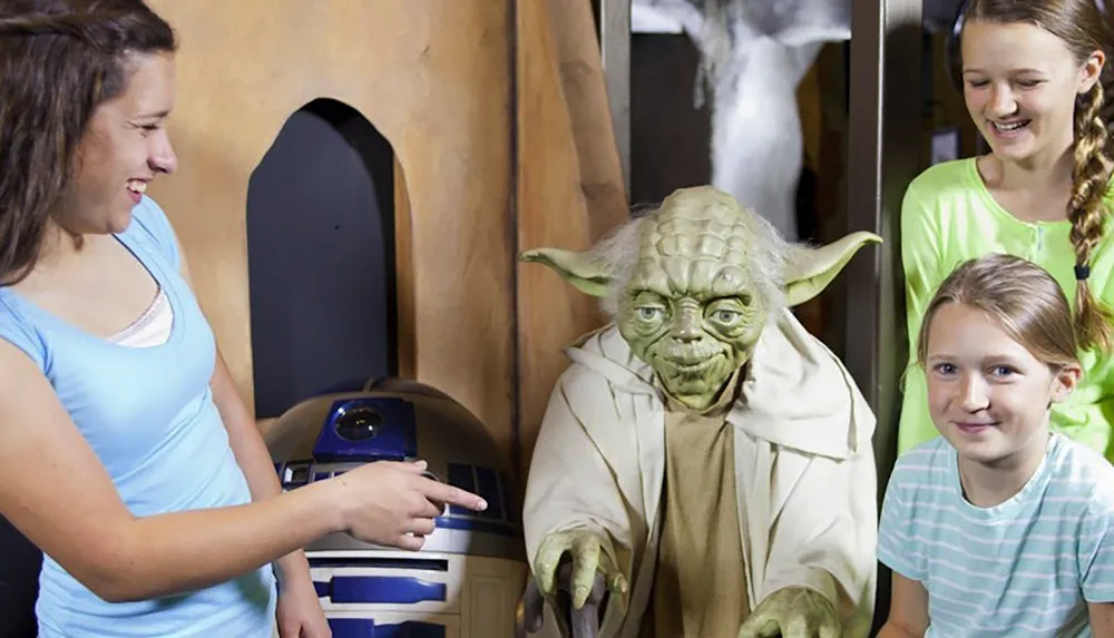 Three people are smiling and posing with figures of Yoda and R2-D2 from Star Wars