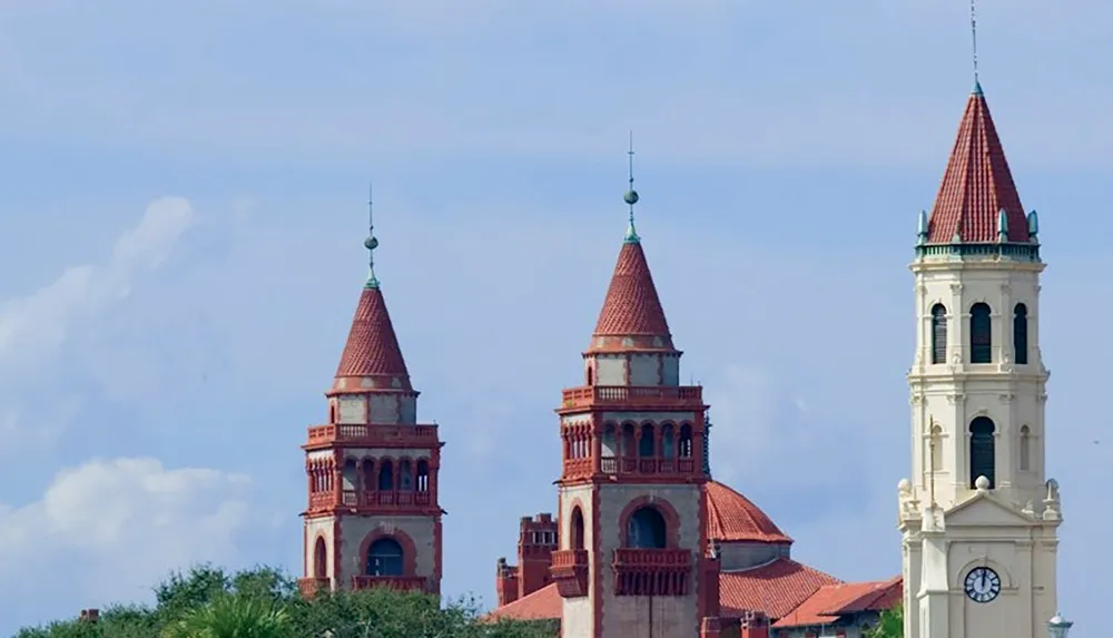 The image features three architectural towers with red roofs and intricate detailing against a backdrop of blue sky